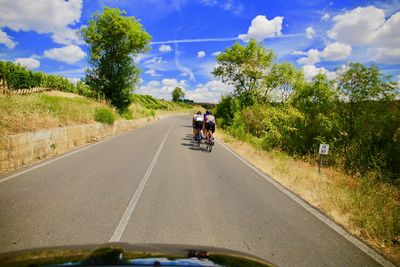 People riding bicycle on road against sky