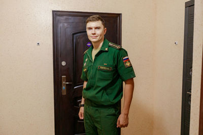 Portrait of man in uniform standing against door