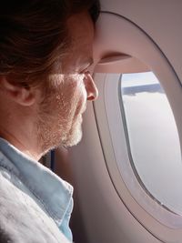 Side view of man looking out of window sitting in airplane 