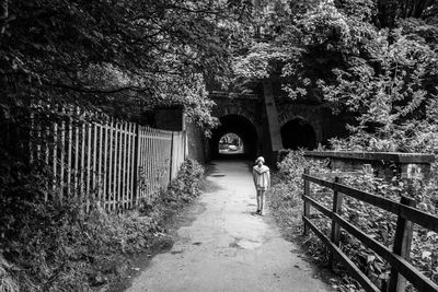 Full length rear view of girl walking on road by plants and trees