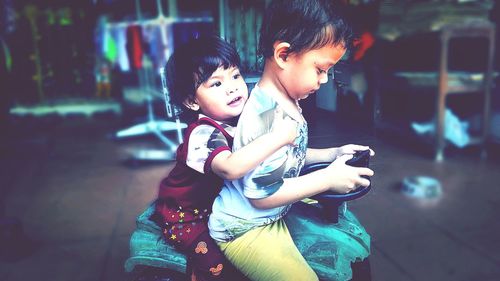 Siblings sitting on toy vehicle at home