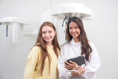 Young woman using mobile phone while standing against wall