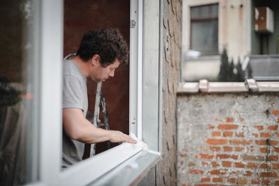 A caucasian man in a gray uniform washes with a dry paper napkin inside the window frame opening