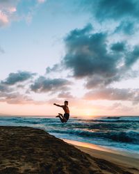 Silhouette man jumping on beach against sky during sunset