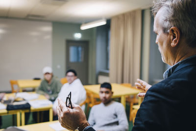 Male teacher gesturing while teaching students in classroom