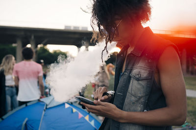 Side view of young man smoking while using mobile phone at music event