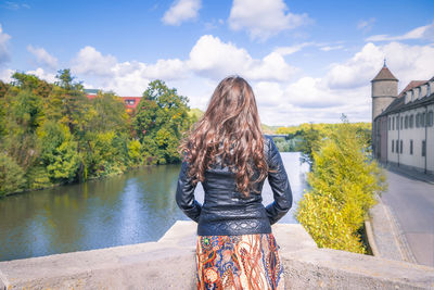 Rear view of young woman standing by building against sky