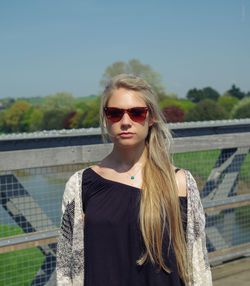 Portrait of young woman wearing sunglasses standing against sky