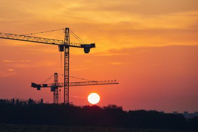 Silhouette cranes at construction site during sunset