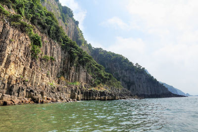 Scenic view of sea by mountain against sky