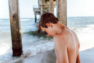 Side view of shirtless boy looking at sea