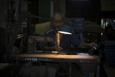 Mature man stitching clothes in workshop