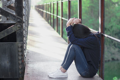 Rear view of woman sitting on railing