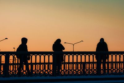 Silhouette people standing by railing against clear sky during sunset