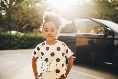 Portrait of girl standing against electric car on driveway