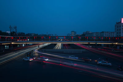 Light trails on bridge in city against sky at night