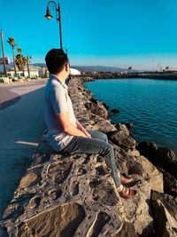 Man sitting on rock over sea against clear sky