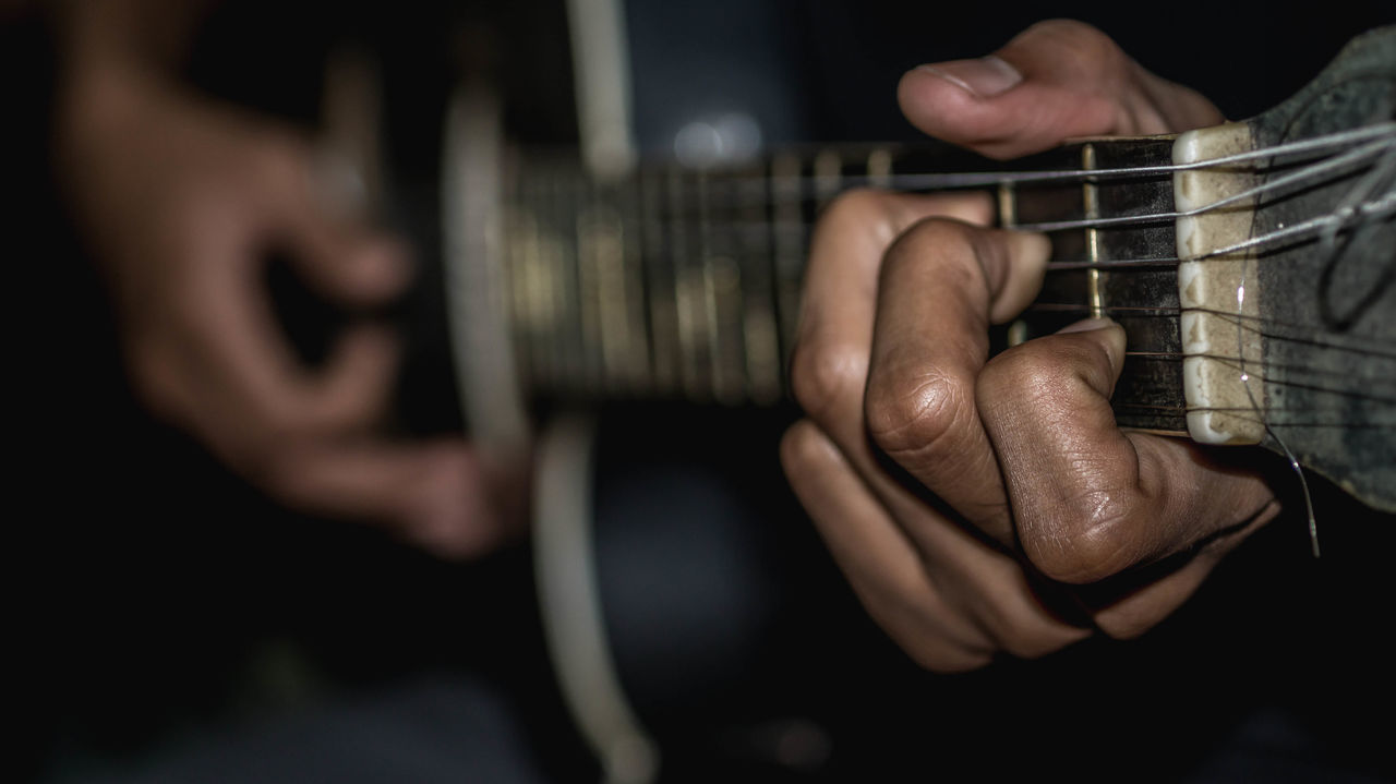 MIDSECTION OF MAN PLAYING GUITAR AT CAMERA