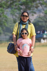 Portrait of smiling young woman with daughter standing on field