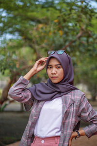 Portrait of young woman standing against trees