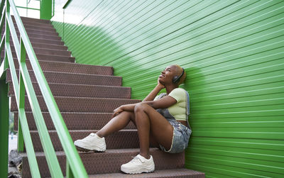 Side view of woman sitting on staircase against wall