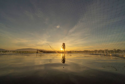 Reflection of woman on sea against sky during sunset