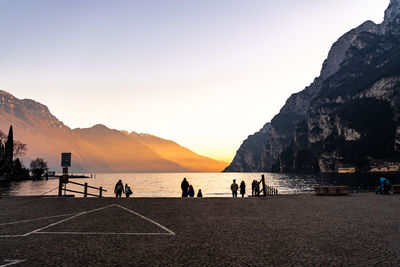 People at lakeshore against mountains during sunset