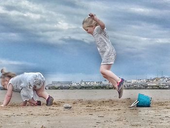 Children playing on sand at beach against sky