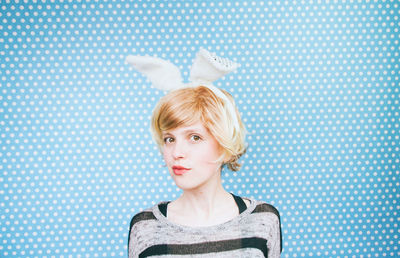 Portrait of young woman wearing costume rabbit ears against blue polka dots wall