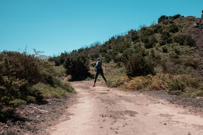 Woman walking on road by trees against clear blue sky