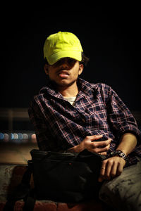 Portrait of young man sitting against black background