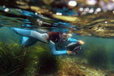 Mid adult woman collecting seafood in bag while diving into sea