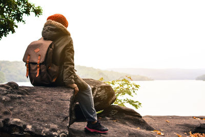 Rear view of boy sitting on rock against lake