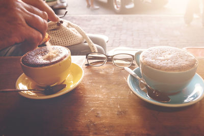Cropped hand adding sugar to coffee on table at cafe