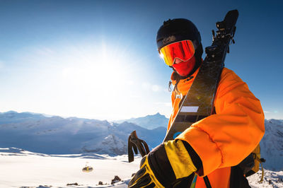 Photo of an athlete in a helmet and mask with skis on his shoulder. a young man stands in the