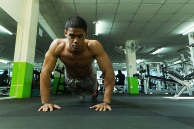 Full length of shirtless man exercising at gym
