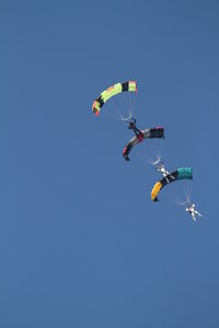 Low angle view of people paragliding against clear blue sky