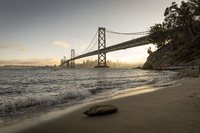 Suspension bridge over sea against sky during sunset