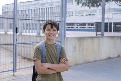 Portrait of boy with arms crossed standing against school