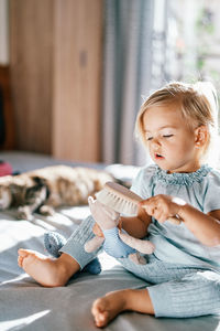 Portrait of cute girl using mobile phone while sitting on bed at home