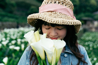 Close-up of smiling young woman holding flower standing at field