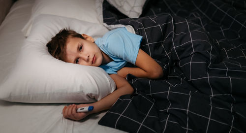 Sick child laying in bed and holding termometer in hand