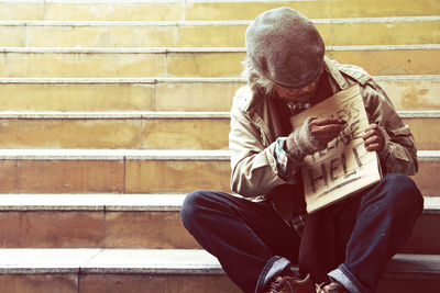 Beggar writing on cardboard while sitting on steps