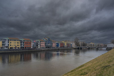 Buildings by river against cloudy sky