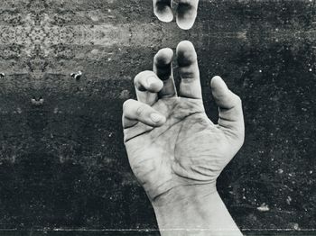 Cropped image of person reaching fingers against wall