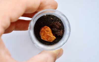 Cropped hand holding rock in jar on white background