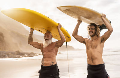 Smiling shirtless men carrying surfboards at beach