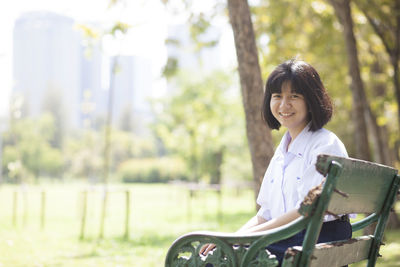 Portrait of smiling woman sitting on bench in park