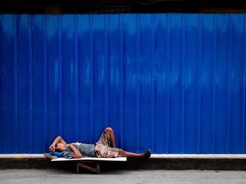 Side view of beggar sleeping against blue metallic wall