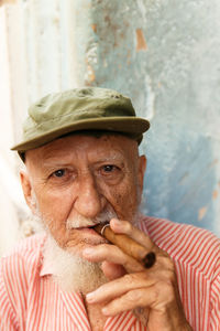 Close-up portrait of senior man wearing cap smoking cigar